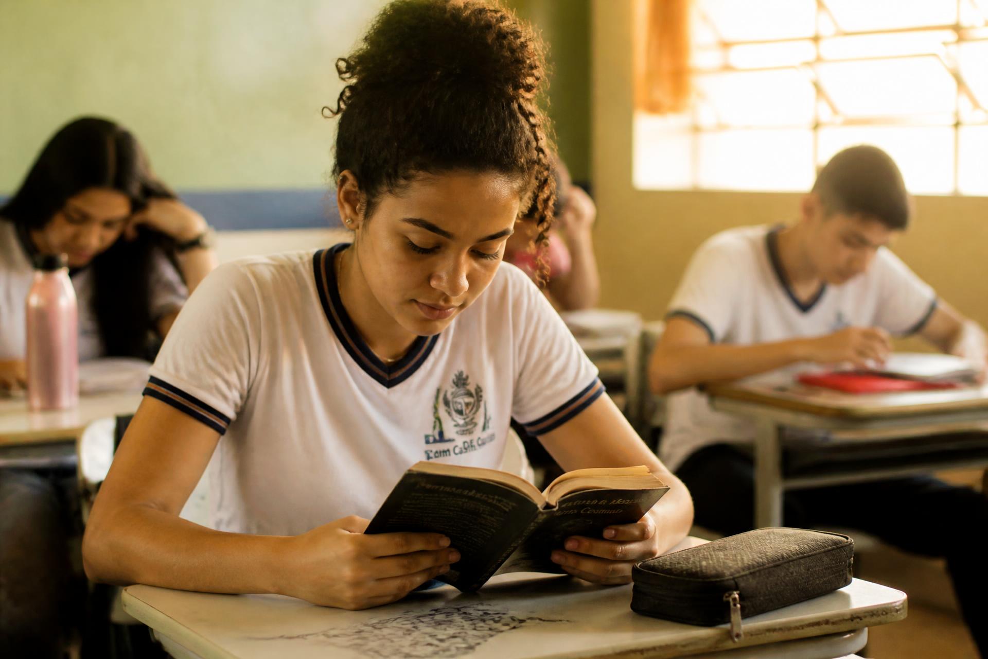 Jovem estudante lendo em sala de aula iluminada por luz natural